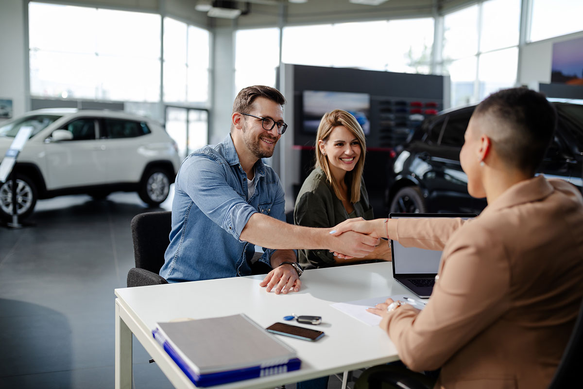 couple making deal with car salesman at car dealership